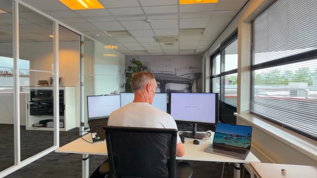 Marc Diks werkt op zijn kantoor achter drie beeldschermen en een laptop, met uitzicht op de straat door het raam.